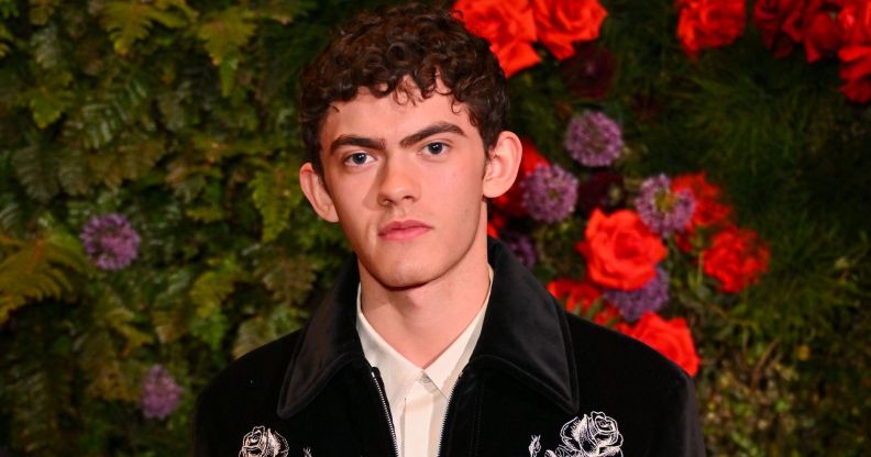 Joe Locke poses in a black jacket and white shirt against a flowery background.