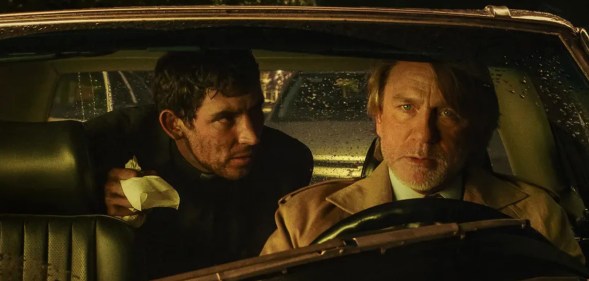 Wake Up Dead Man: A Knives Out Mystery still: Daniel Craig in the driver's seat with Josh O'Connor leaning from the back seat to speak to him.