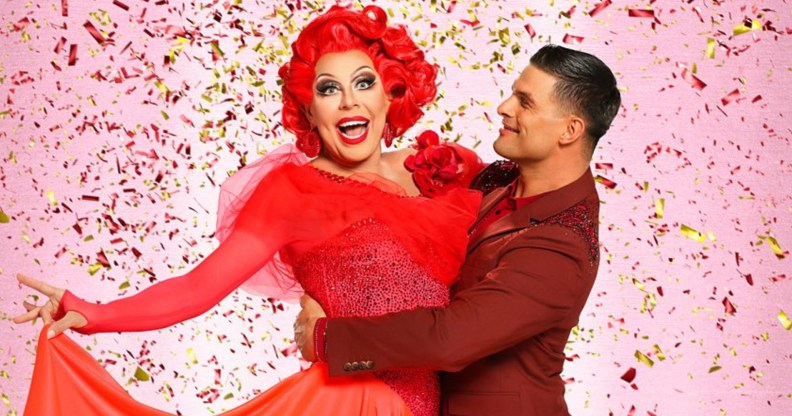 La Voix with red hair and red sequined earings and dress being held by her dance partner, Aljaz Škorjanec, in a maroon suit.