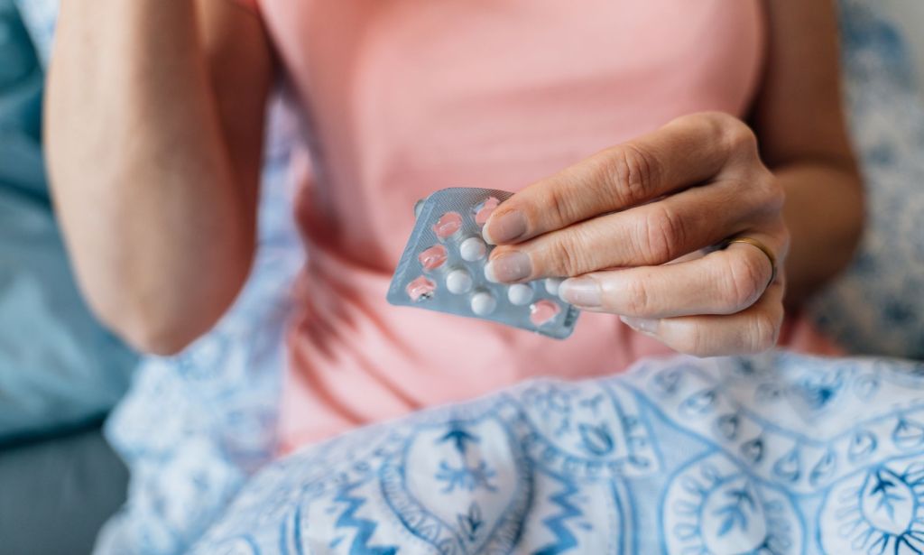 A person taking HRT pills while holding a tablet packet.