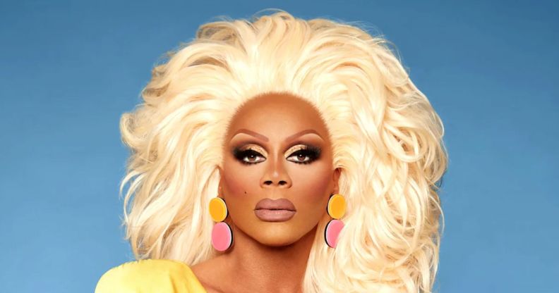 RuPaul poses in a yellow dress with yellow and pink earrings.