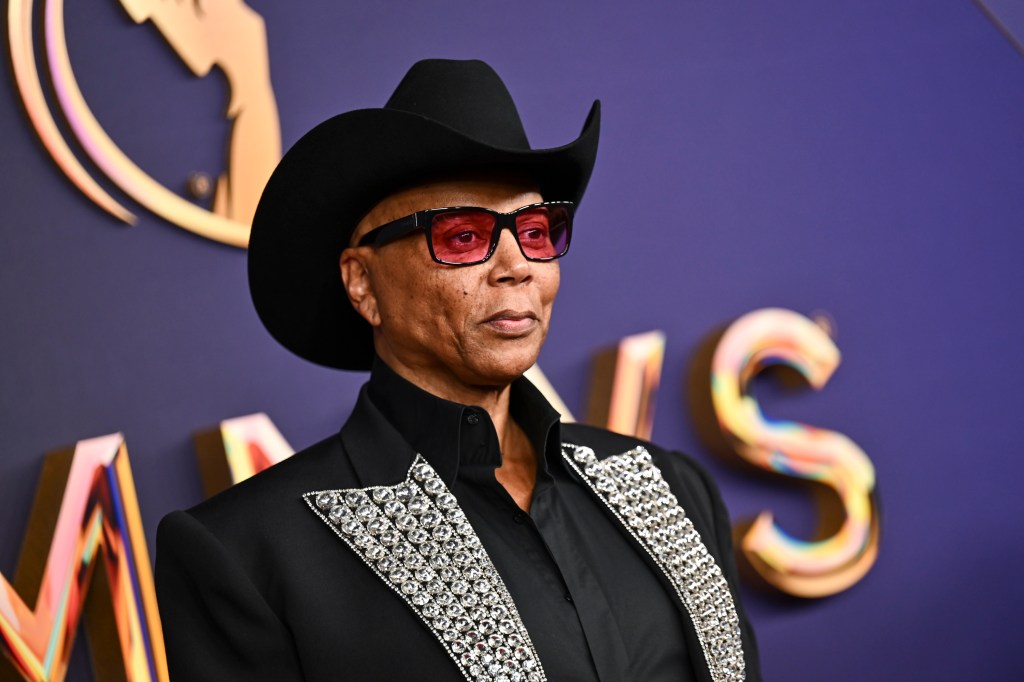 RuPaul at the 76th Primetime Emmy Awards. He's wearing a black cowboy hat and suit with silver lapels and red glasses.