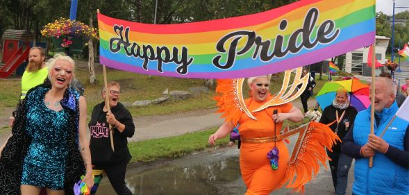A photo from Senja Pride featuring smiling participants and drag queens holding a banner that says Happy Pride.
