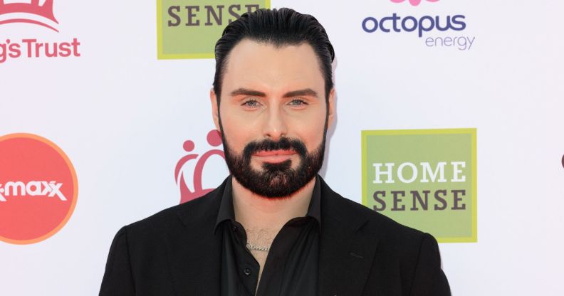 Rylan Clark smiles on a red carpet wearing a black shirt.