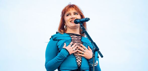 CMAT performs in a blue laced up top and places her hands to her chest as she looks off to the right.
