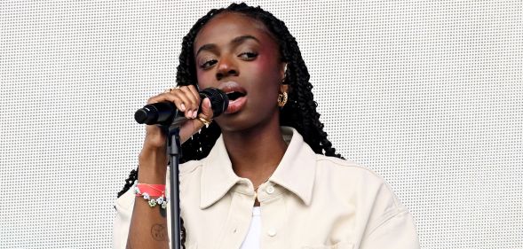 Cat Burns in a cream shirt holding a microphone singing.