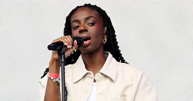 Cat Burns in a cream shirt holding a microphone singing.