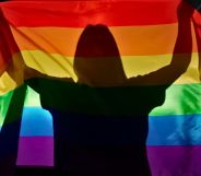 A silhouette holding an LGBTQ+ Pride flag.