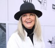 Diane Keaton in a white jacket and black hat laughing.