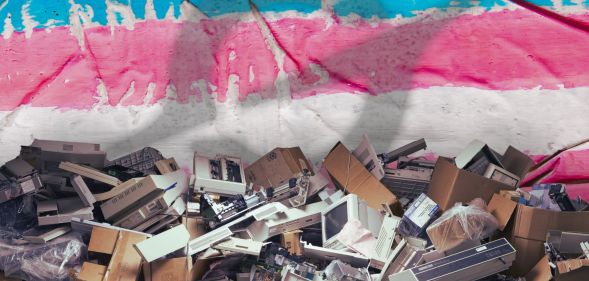 A pile of broken tech edited in front of a trans flag with the Grok logo superimposed over it.