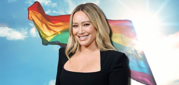Hilary Duff smiles wearing a black top, imposed against a rainbow flag billowing in the sky.