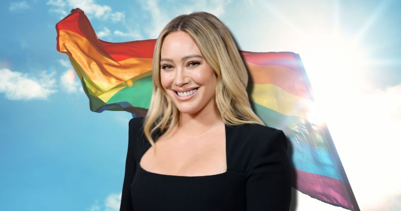 Hilary Duff smiles wearing a black top, imposed against a rainbow flag billowing in the sky.