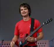 Djo performs in a red t-shirt and holds a guitar.