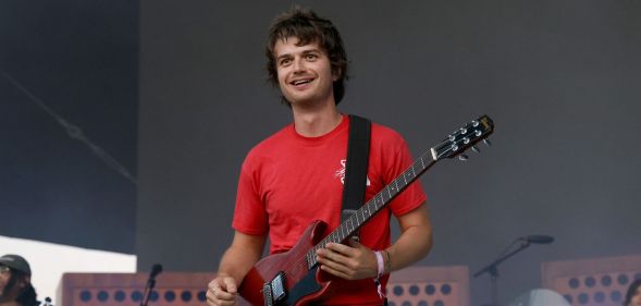 Djo performs in a red t-shirt and holds a guitar.