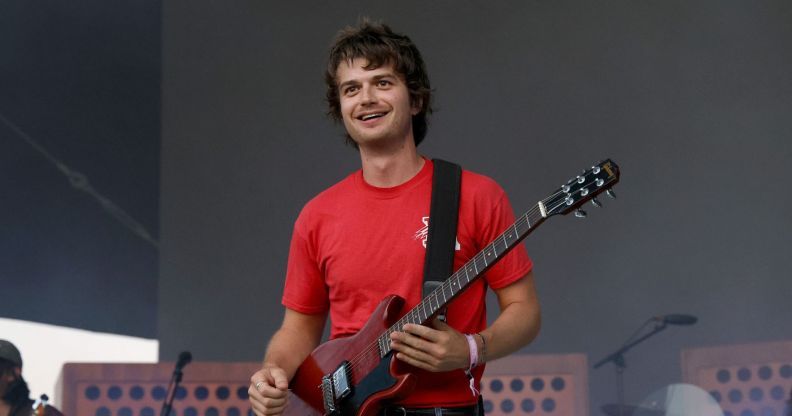 Djo performs in a red t-shirt and holds a guitar.