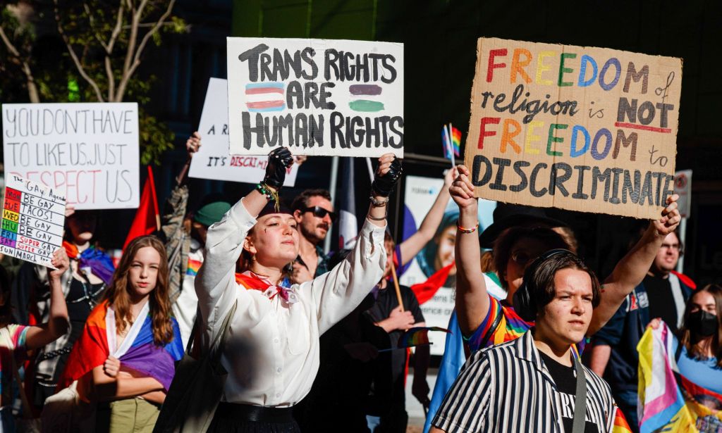 Protestors in Australia holding signs promoting LGBTQ+ rights.