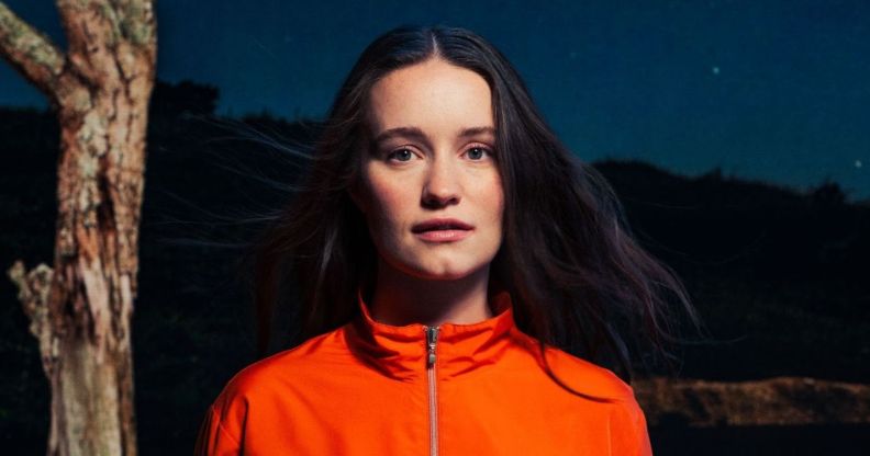 Sigrid looking at the camera, wearing an orange zip neck jumper.