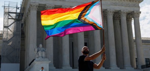 Someone holding an LGBTQ+ flag outside the Supreme Court.