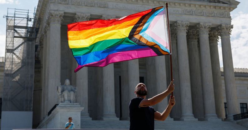 Someone holding an LGBTQ+ flag outside the Supreme Court.