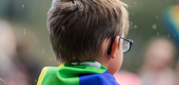 A child with a Pride flag on their shoulders.