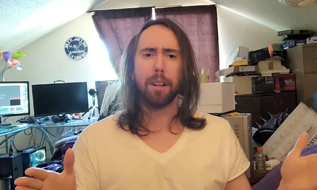 A picture of Asmongold speaking to a webcam inside his messy, messy room.