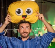 Jonathan Bailey holding a cuddly emoji smile cushion above his head