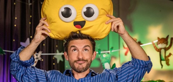 Jonathan Bailey holding a cuddly emoji smile cushion above his head