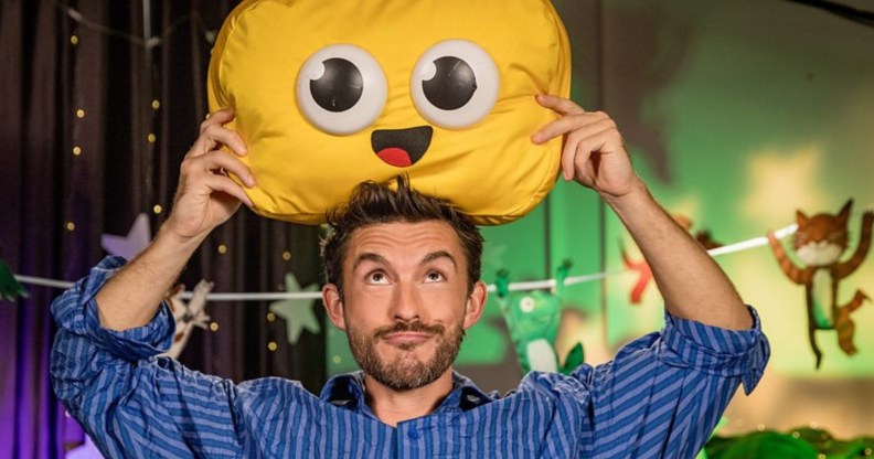 Jonathan Bailey holding a cuddly emoji smile cushion above his head