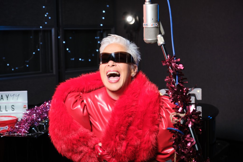 Denise Welch in all red and sunglasses, laughing close to a microphone.