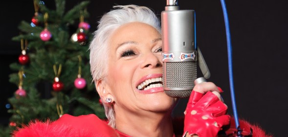 Denise Welch in all red, smiling close to a microphone. Christmas tree in the background