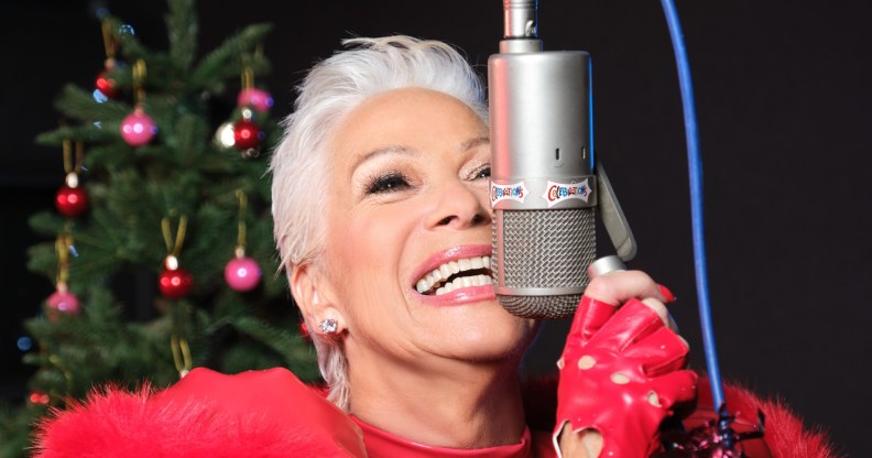Denise Welch in all red, smiling close to a microphone. Christmas tree in the background