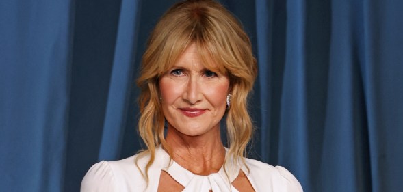 Laura Dern against a blue curtain background wearing a white dress.