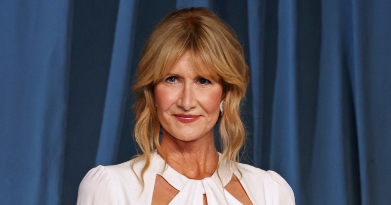 Laura Dern against a blue curtain background wearing a white dress.