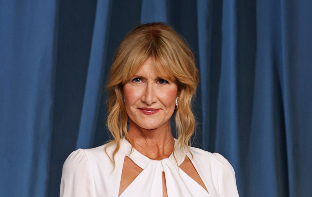 Laura Dern against a blue curtain background wearing a white dress.