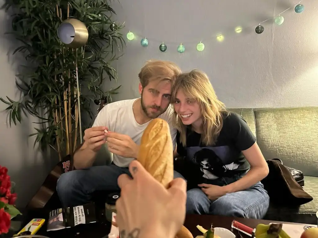 Christian Lee Hutson and Maya Hawke posing together, photo taken by their friend, who's holding a baguette in the shot