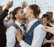 Two men kiss surrounded by a crowd of people throwing confetti.