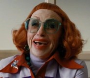 Weapons still of Aunt Gladys with bright red hair and micro-bangs, smudged red lipstick and bright teal glasses.