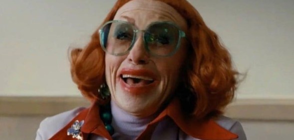 Weapons still of Aunt Gladys with bright red hair and micro-bangs, smudged red lipstick and bright teal glasses.