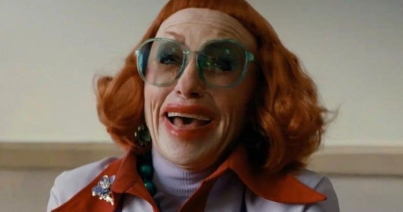 Weapons still of Aunt Gladys with bright red hair and micro-bangs, smudged red lipstick and bright teal glasses.