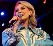 A blonde woman holding a microphone in a blue shirt.