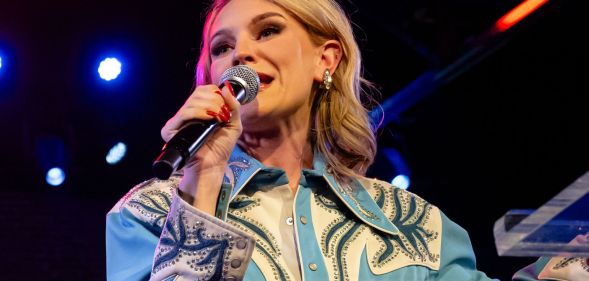 A blonde woman holding a microphone in a blue shirt.
