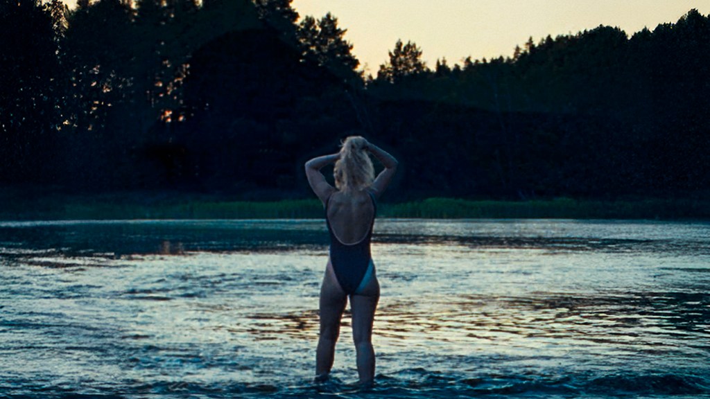 The Chronology of Water, a woman with her back to the camera tying her hair up as she swims in a lake