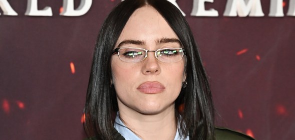 Billie Eilish in small glasses, a light blue shirt and green jacket