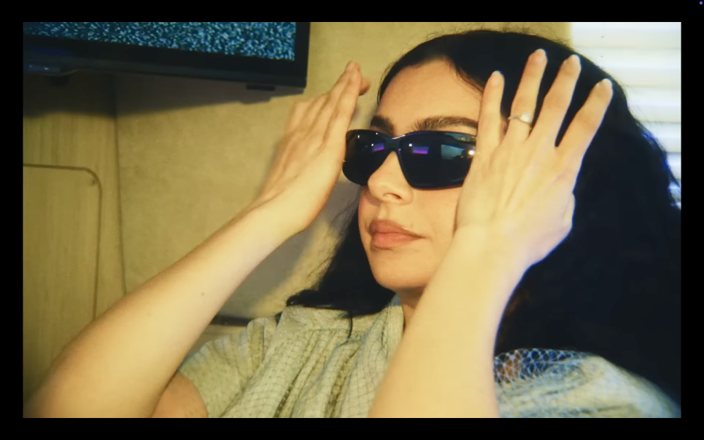 Charli XCX putting on black sunglasses in The Moment