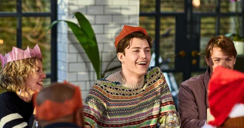 Cheerful young man wearing Christmas cracker hat playing after dinner games with family.