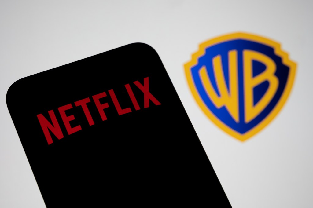 In this photo illustration, the Netflix logo appears on a cell phone with the Warner Bros. logo in the background, in Creteil, France, on December 10, 2025. (Samuel Boivin/NurPhoto via Getty Images)