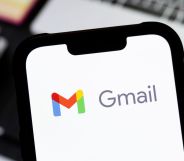 Someone holding a phone in front of a laptop with the Gmail logo visible.
