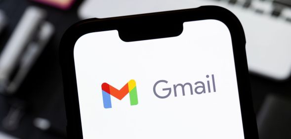 Someone holding a phone in front of a laptop with the Gmail logo visible.