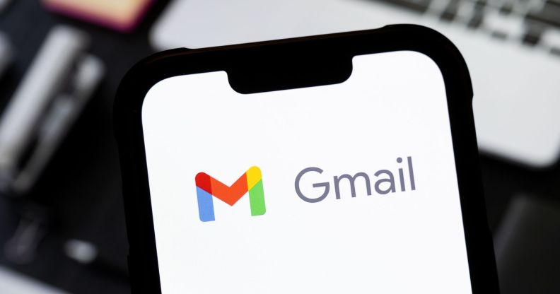 Someone holding a phone in front of a laptop with the Gmail logo visible.