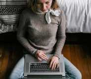 Girl sits on the floor with a laptop over her legs.